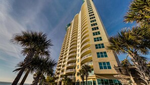 A tall, multi-story hotel with balconies and large windows, surrounded by palm trees.