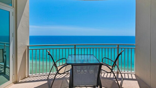 A balcony with a table and chairs, overlooking a clear blue ocean.