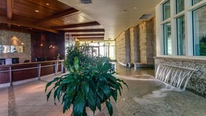 A lobby with a reception desk, a large indoor waterfall, and a reception area with a stone wall and large windows.