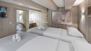 A modern hotel room with wooden walls and ceiling, a large bed with white linens, a painting of a snowy landscape, and a bathroom with a mirror and sink. - Renovated top-floor apartment with slope access, sleeps 6 (Courchevel 1650)