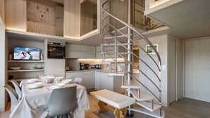 A modern kitchen with a built-in oven, a dining area with a round table and chairs, and a spiral staircase leading to an upper level. - Renovated top-floor apartment with slope access, sleeps 6 (Courchevel 1650)