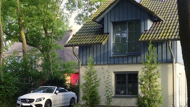 Een witte auto geparkeerd voor een huis met een pannendak en een raam.