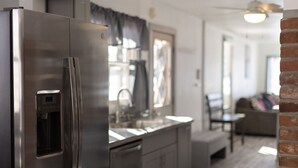Una cocina moderna con un refrigerador de acero inoxidable, dispensador de agua integrado y un lavamanos. En el fondo, hay una zona de comedor con una mesa y sillas.