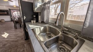 Cocina moderna con dos fregaderos de acero inoxidable, una cafetera y un ventanal con vistas a árboles.