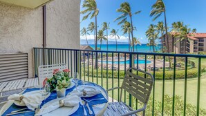 Un balcone con tavolo apparecchiato per mangiare, vista su una piscina e una spiaggia con palme.