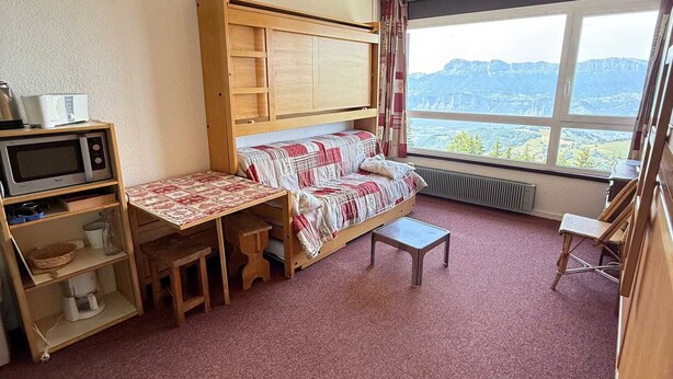 Habitación pequeña con literas, una mesita, microondas y vistas a las montañas a través de un ventanal grande.