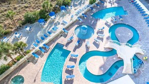 Vue aérienne d’un complexe hôtelier doté de plusieurs piscines, de chaises longues et d’un toboggan aquatique.