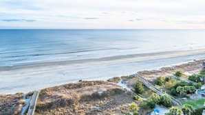 Une vue sur la côte, avec une plage, une promenade en bord de mer et un bâtiment auquel mène un chemin.