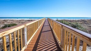 A wooden boardwalk leading to a beach with a clear blue sky.
