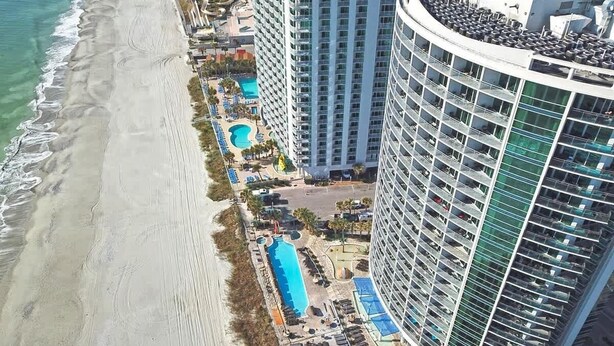 A high-rise hotel with a pool area, beach access, and multiple balconies. - Coastal condo with balcony & beach access (Myrtle Beach)