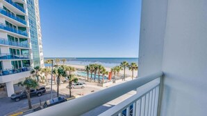 A high-rise hotel with a balcony overlooking a beach, palm trees, and a swimming pool. - Coastal condo with balcony & beach access (Myrtle Beach)
