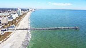 A coastal cityscape with a long pier extending into the ocean, surrounded by buildings and a beach. - Coastal condo with balcony & beach access (Myrtle Beach)