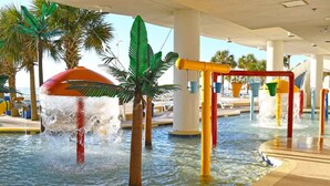 A water play area with multiple water jets and a slide, surrounded by palm trees and a pool. - Coastal condo with balcony & beach access (Myrtle Beach)