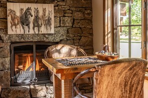 A stone fireplace with a fire, a chessboard, and a painting of horses.
