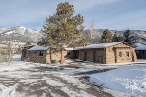 A stone building with a snow-covered roof, surrounded by trees and mountains.