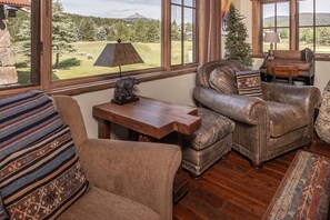 Una sala de estar acogedora con un sillón de cuero, una mesa de centro de madera y vistas a un paisaje montañoso a través de grandes ventanales.