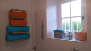A bathroom with a towel rack holding multiple towels, a window with a view of greenery, and a metal rack with bags.