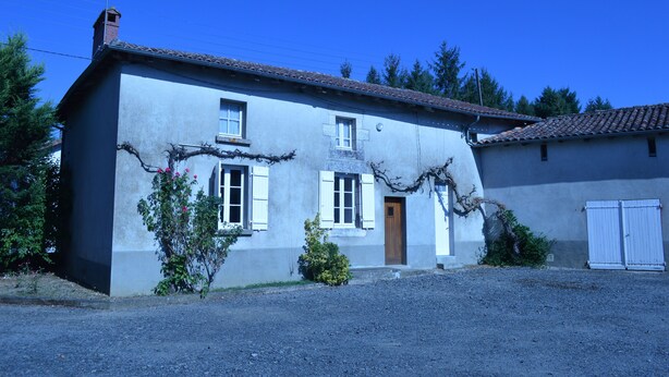 A two-story house with a gravel driveway, a wooden door, and a small garden area.