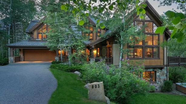 En tvåvånings timmerstuga med en grund av sten, stora fönster och en välskött trädgård.