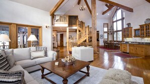 Ett rymligt vardagsrum med en trätrappa, en matplats och ett kök med träskåp.