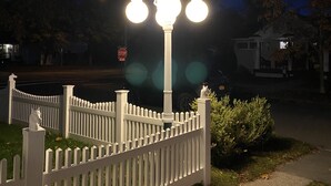 Una cerca blanca con una farola que tiene tres luces esféricas y una estatua de un caballo.