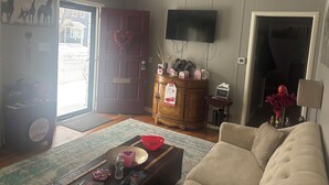 Una sala de estar con un sofá, una mesa de centro, un mueble de madera, un televisor montado en la pared y una puerta decorada con un corazón.