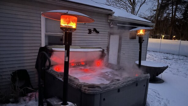 Jacuzzi con dos calentadores, rodeado de nieve, junto a una casa.