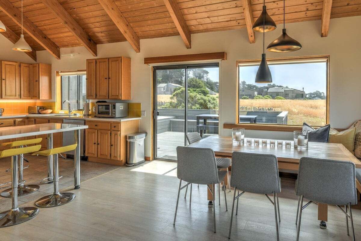 A modern kitchen with wooden cabinets, a stainless steel bar, and a large window overlooking a grassy area.