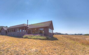 A modern house with a large porch, surrounded by a grassy field.