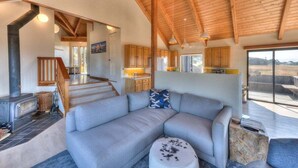 Un intérieur moderne avec un grand canapé d’angle, une cheminée, des poutres en bois et un coin cuisine.