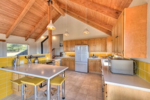 Una cocina con armarios de madera, una isla central con taburetes altos e iluminación colgante.
