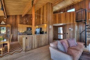 A spacious interior with a central kitchen, a dining area, and a living space with a sofa. - Beach Walk | Dog-Friendly Getaway with Hot Tub (Sea Ranch)