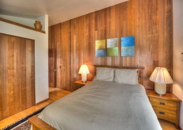A bedroom with a wooden panel wall, a bed with white linens, two bedside lamps, and a small table.