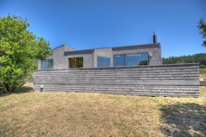 A modern house with a sloped roof, large windows, and a chimney. - Beach Walk | Dog-Friendly Getaway with Hot Tub (Sea Ranch)