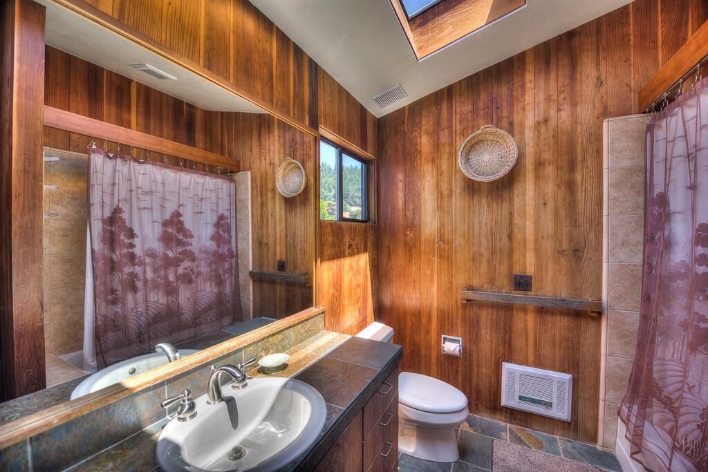 A bathroom with a wooden wall, a sink with a mirror, a toilet, and a shower curtain.