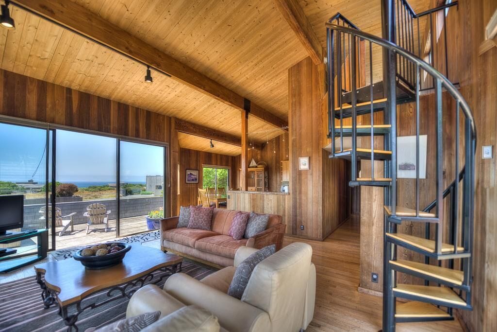 A spacious living area with a large window, a sofa set, a coffee table, and a spiral staircase.