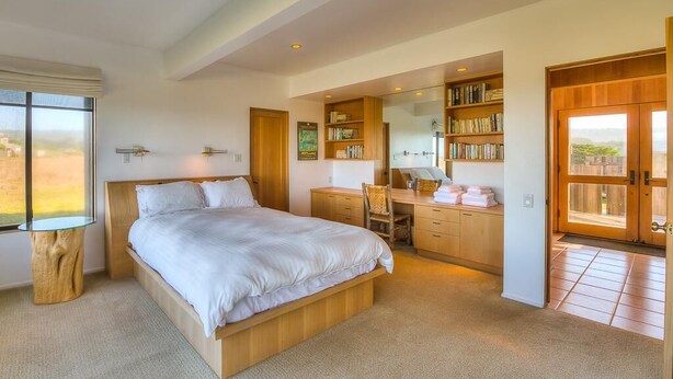 A bedroom with a large bed, a desk, and a bookshelf. - Berk | Ocean Views, Fireside Nights & Hot Tub (Sea Ranch)