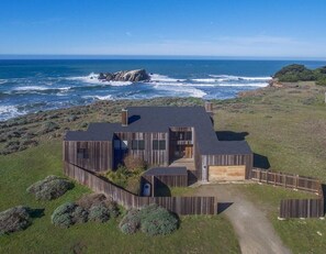 A coastal house with a large garage, a covered porch, and a view of the ocean. - Berk | Ocean Views, Fireside Nights & Hot Tub (Sea Ranch)