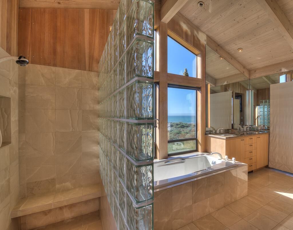 A modern bathroom with a glass shower enclosure, a large window with a view, and a wooden vanity.