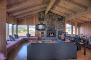 A cozy living room with a stone fireplace, a large gray sofa, and a television. - Berk | Ocean Views, Fireside Nights & Hot Tub (Sea Ranch)