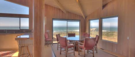 A modern interior with a large dining table, chairs, and a view of the ocean.