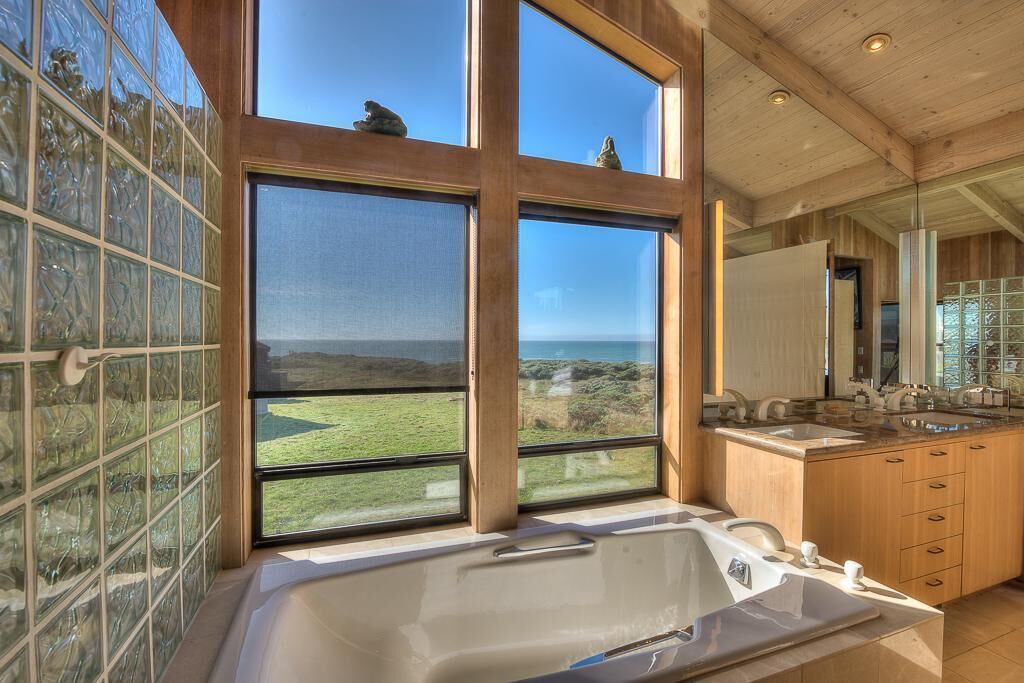 A modern bathroom with a large bathtub, wooden cabinetry, and a view of the landscape through large windows.
