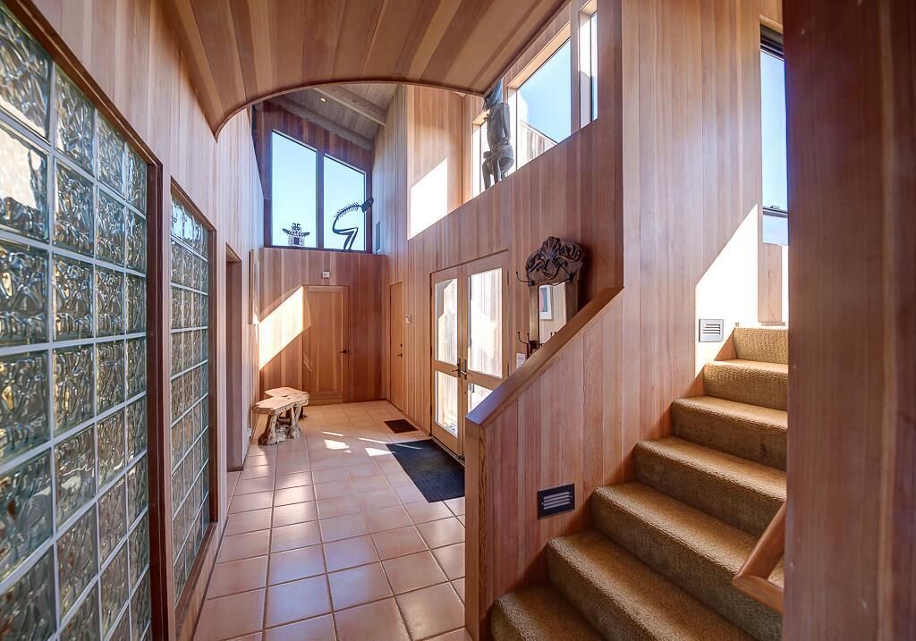 Un intérieur en bois avec un escalier, une porte en verre ornée d’un motif décoratif et une petite table.