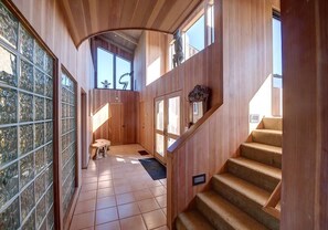 A wooden interior with a staircase, a glass door with a decorative pattern, and a small table. - Berk | Ocean Views, Fireside Nights & Hot Tub (Sea Ranch)