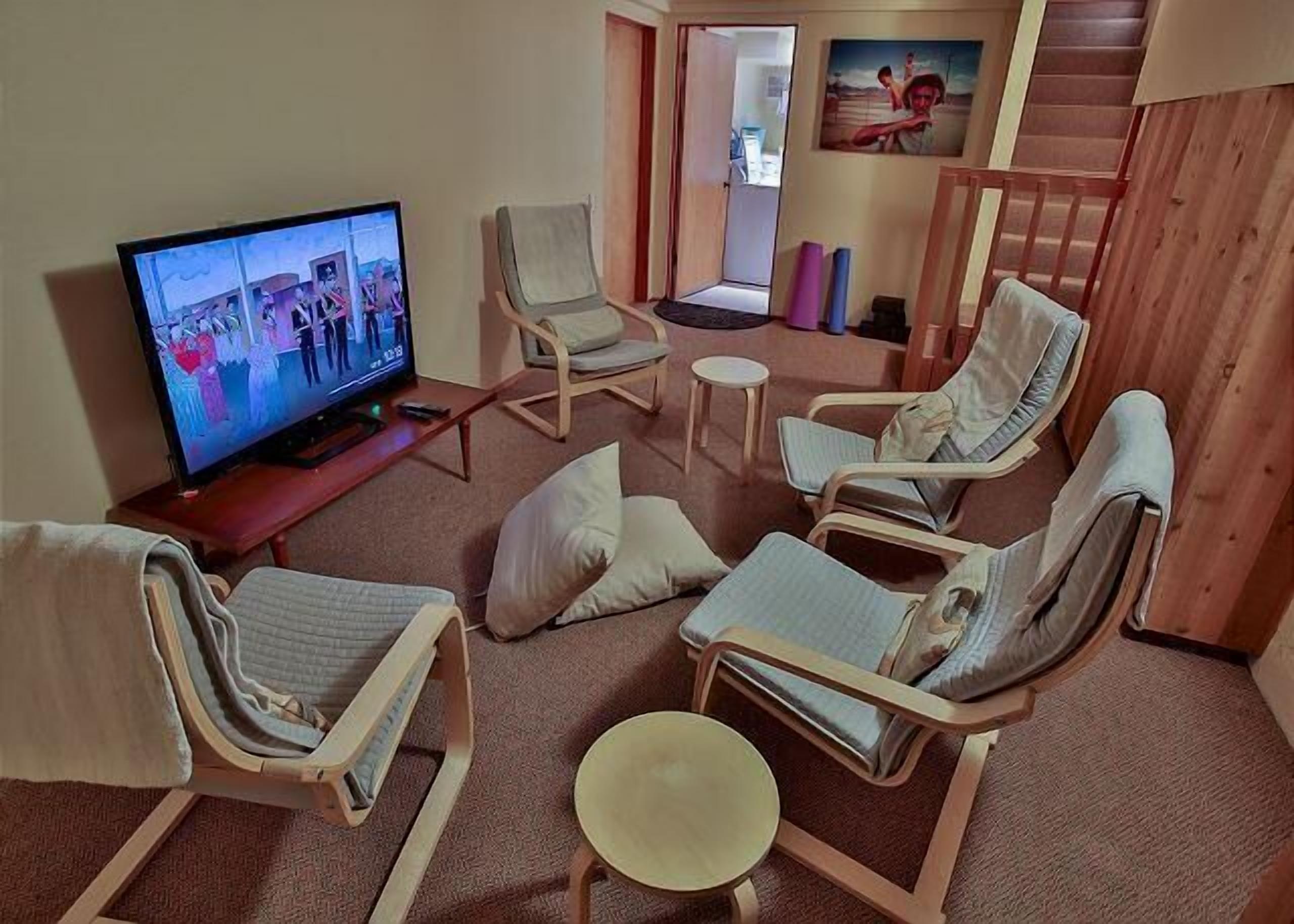 A living room with a television, reclining chairs, a small table, and a staircase.