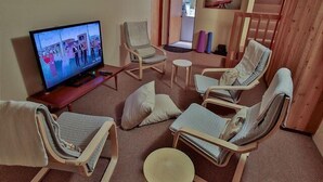 Een woonkamer met een televisie, loungestoelen, een bijzettafeltje en een trap.