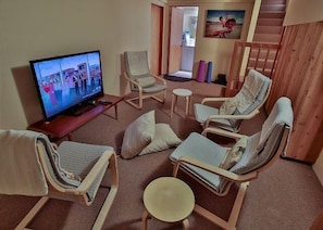 A living room with a television, reclining chairs, a small table, and a staircase. - Forest House | Tranquil Escape & Trails (The Sea Ranch)
