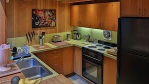 Een kleine keuken met houten kastjes, een fornuis, een spoelbak en een koelkast.