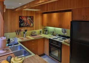 A compact kitchen with wooden cabinets, a stove, a sink, and a refrigerator. - Forest House | Tranquil Escape & Trails (The Sea Ranch)