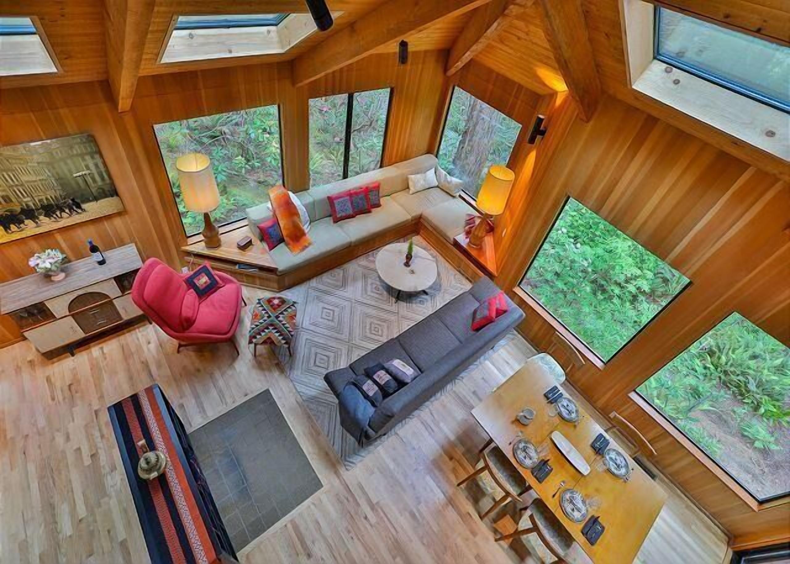 A spacious room with a large window, a sofa, a dining table, and a red chair.